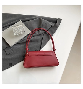 Detail of burgundy rectangular underarm bag with thin shoulder straps on white surface