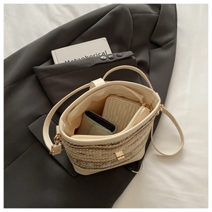 Detail of beige woven bucket bag featuring zipper closure and leather shoulder strap