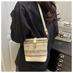 Detail of woven bucket bag with adjustable leather strap and golden turn-lock closure