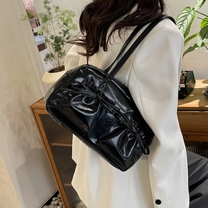Gros plan d'un sac à bandoulière noir brillant avec nœuds sur un blazer blanc