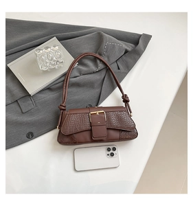 Detailed view of brown crocodile-embossed baguette bag with large gold buckle and shoulder strap