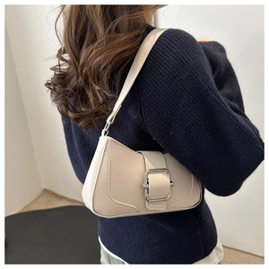 Detail of a creamy beige baguette shoulder bag with a large silver buckle on a model