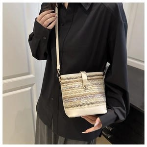 Detail of woven straw bucket bag with white leather trim and metal clasp on a model