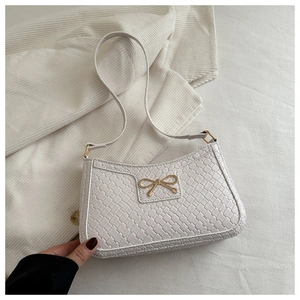 Détail d'un sac à bandoulière tressé blanc avec fermoir nœud doré sur tricot