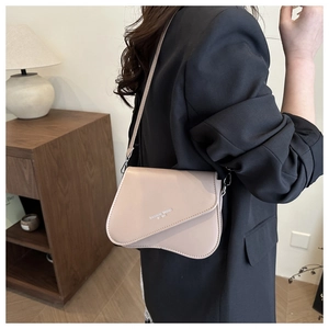 Detail of light apricot leather crossbody bag featuring an asymmetric flap and fashion text