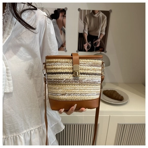 Detail of woven straw bucket bag featuring contrast stripes and gold metal lock