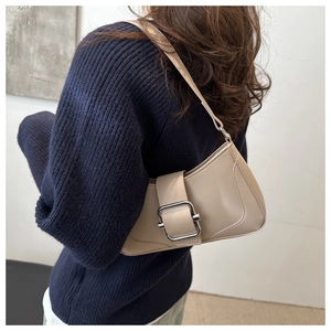 Detail view of a beige minimalist hobo bag with a large silver buckle on a blue sweater
