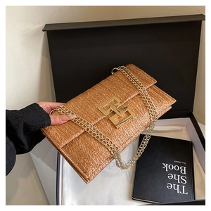 Detail of a brown woven straw handbag with a gold geometric clasp in a gift box