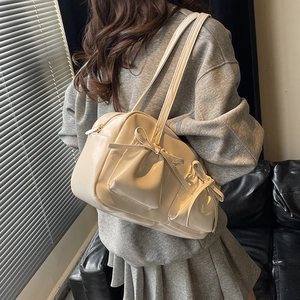 Sac fourre-tout crème brillant avec nœud et poches latérales porté par un mannequin