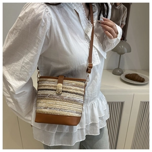 Detail of woven straw bucket bag with brown leather trim and gold metal buckle