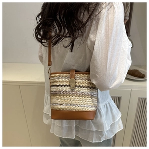 Detail of woven bucket bag featuring brown leather straps and gold metal twist-lock