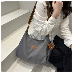 Detailed side view of grey nylon shoulder bag with brown fabric strap worn by a model