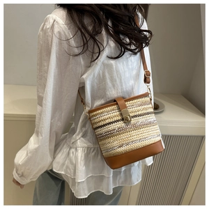 Detail of woven brown straw bucket bag with leather strap worn by a female model