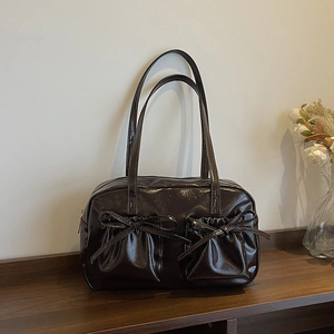 Détail du sac Boston marron brillant avec deux poches frontales et nœuds décoratifs
