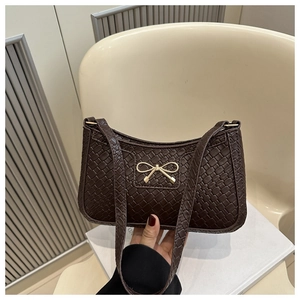 Détail du sac baguette marron foncé tissé avec une boucle nœud dorée élégante en main