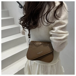 Brown leather saddle bag with adjustable strap worn by model on a white staircase
