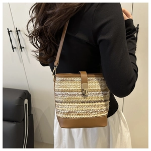 Detail of a woven bucket bag with leather trim and gold rotary lock on a model shoulder