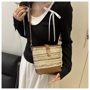 Detail of woven straw bucket bag with brown leather trim worn by a model in casual style