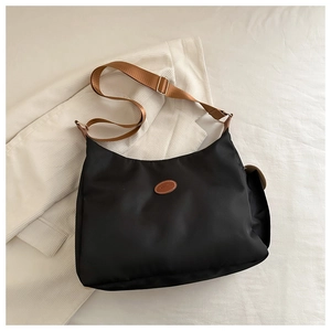 Top-down view of a black nylon crossbody bag with brown leather patch and adjustable strap