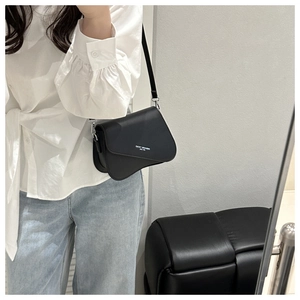 Detail of black faux leather crossbody bag featuring unique asymmetrical flap and slogan print
