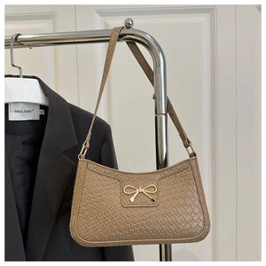 Détail de la texture en cuir tressé et boucle en nœud doré sur un sac à bandoulière marron