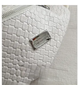 Close-up of white woven faux leather texture and silver fashion metal plaque on chest bag
