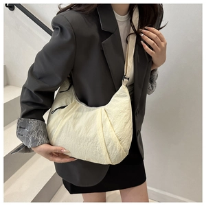 Gros plan d'un sac demi-lune plissé en nylon crème porté par un mannequin dans un décor