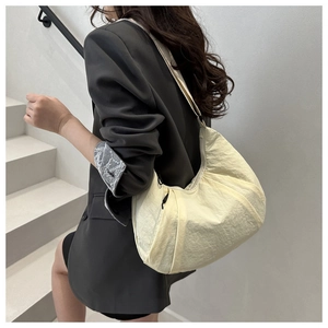 Vue détaillée du sac croissant en nylon crème à texture plissée porté par le mannequin