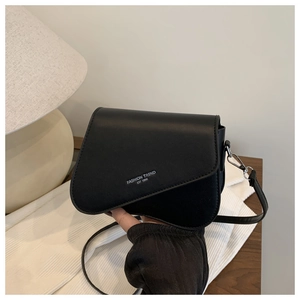 Detail view of the asymmetrical flap design and printed text on a black crossbody bag