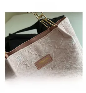 Close-up of pink canvas bag with floral embroidery, textured fabric, and gold chain strap