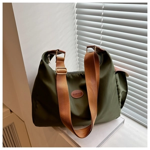 Detail of olive green nylon bag with brown strap leaning on white books by shutters
