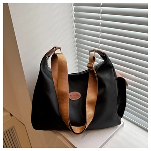 Close-up of a black nylon tote bag with brown straps and 'FASHION' leather patch