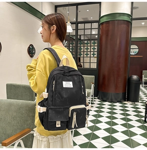 Side view of a black multi-pocket student backpack with beige straps in a stylish cafe