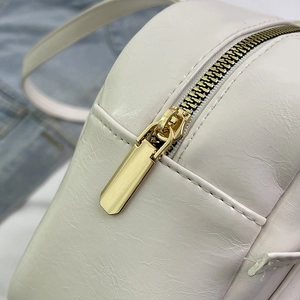 Gros plan sur la fermeture éclair dorée et le cuir blanc texturé du sac fourre-tout