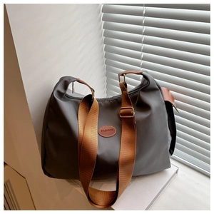 Detail of grey crossbody tote bag with wide brown strap and fashion logo patch