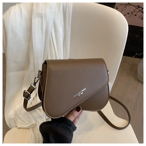 Detailed view of a brown leather crossbody bag with letter print on a white chair