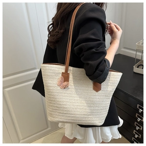 Detail of a beige woven tote with brown leather straps and a pink 3D butterfly charm