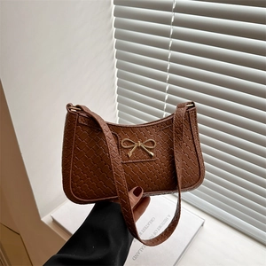 Sac à bandoulière marron tressé avec fermoir nœud doré sous une lumière naturelle