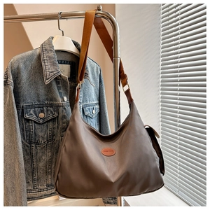 Close-up of a taupe shoulder bag with a silk-like finish and wide caramel strap