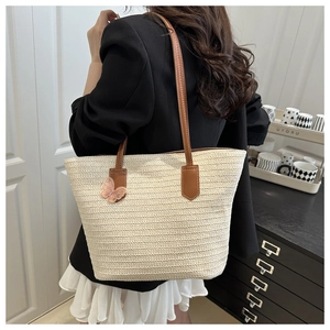 Detail of woven straw tote bag featuring brown leather straps and pink mesh bow charm