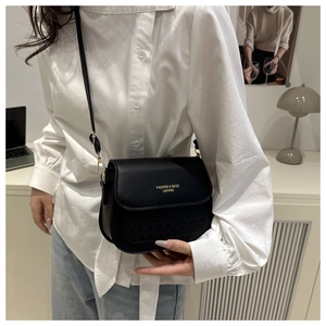 Detail of black leather crossbody bag featuring gold lettering and monogrammed flap texture