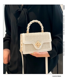 Detail of cream woven handbag featuring golden clover clasp and twisted handle textures