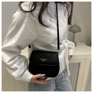 Model wearing a black leather crossbody bag with gold text and thin shoulder strap