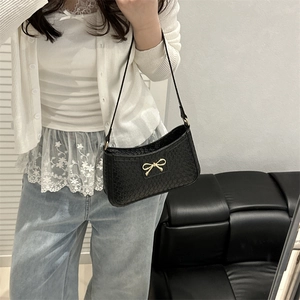 Petit sac carré noir tissé avec fermoir nœud doré tenu par un mannequin pour un look chic