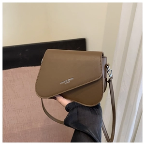 Detail of a brown leather shoulder bag featuring silver text and adjustable strap