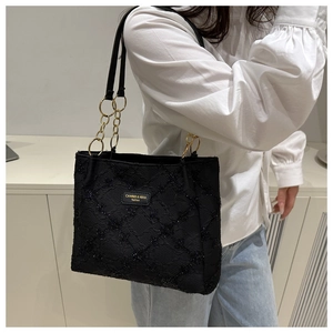 Detail shot of black quilted tote bag with golden metal chain and brand label