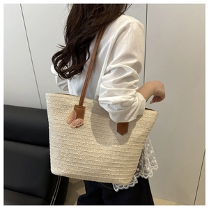 Detail of woven straw tote bag featuring brown leather straps and pink lace butterfly accent