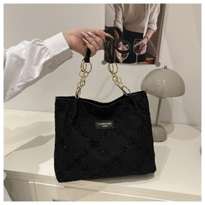 Close-up of black quilted tote bag with chunky gold chain handle and brand tag detail