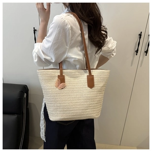 Close-up of woven straw tote bag featuring brown leather handles and a pink mesh butterfly
