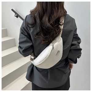Close-up of white woven crossbody bag with silver hardware and wide textile strap
